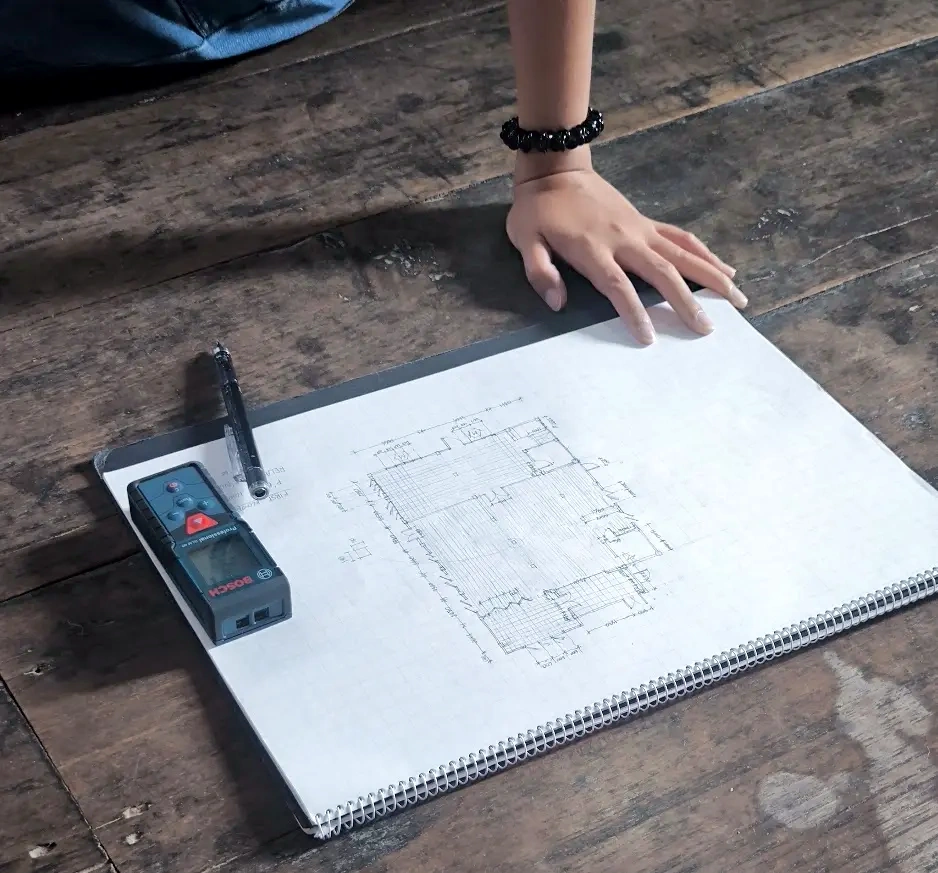 A student documenting a building interior with a sketchbook and laser measure