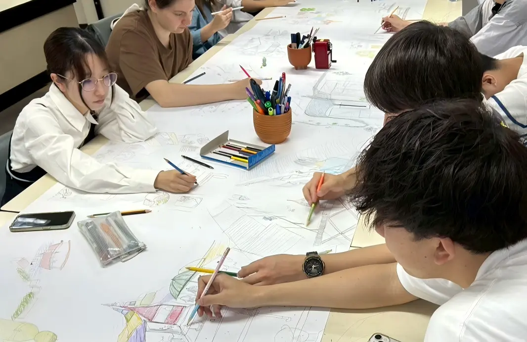 Students and tutors collaborating around a long drawing table in the design studio